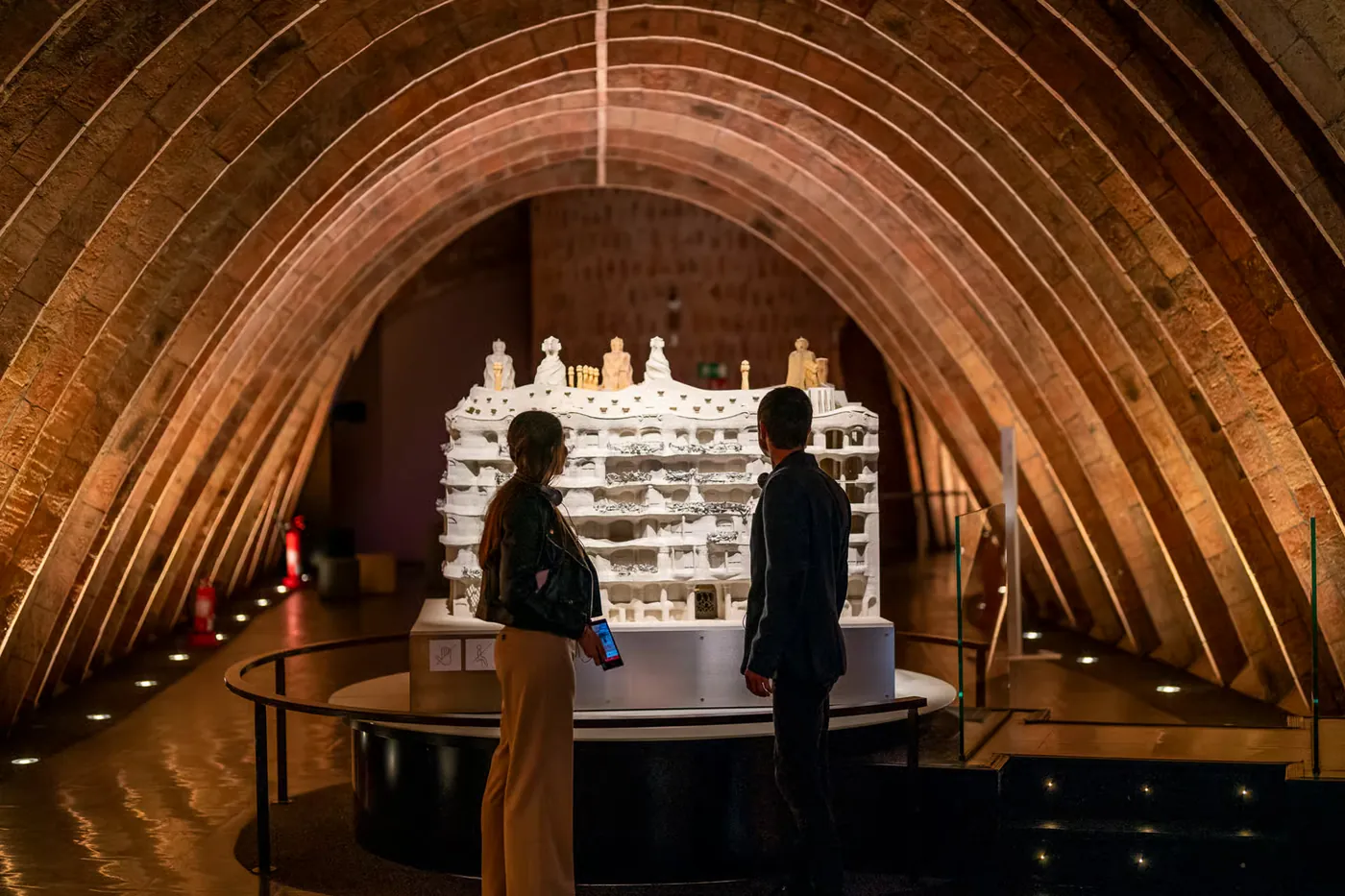 A visitor looks at a scale model beneath the curved brick arches of Casa Mila attic.
